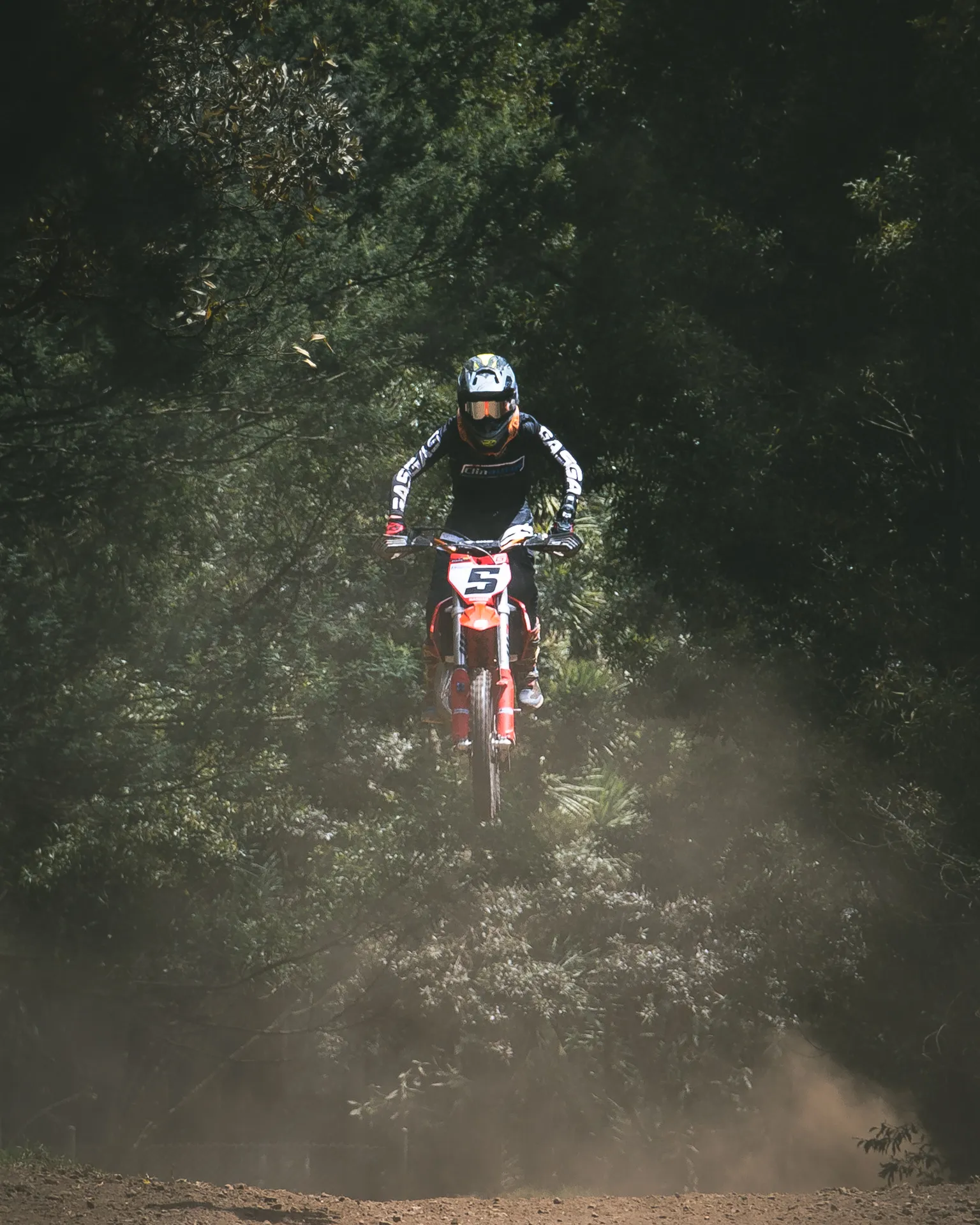 A distant rider rises through dust on a tree-lined circuit.