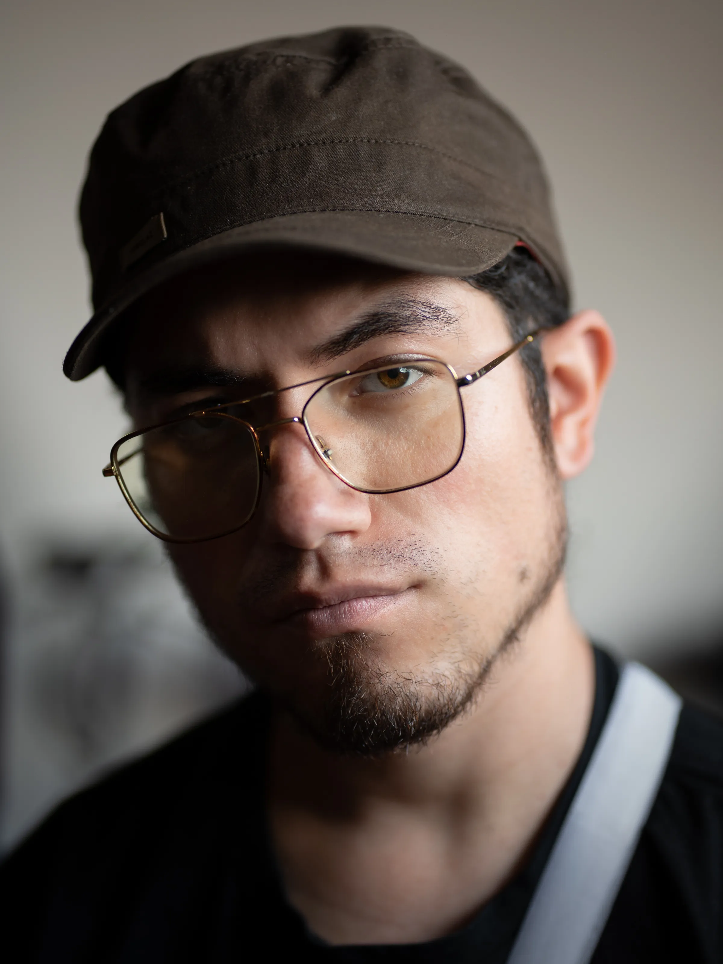 A man with glasses and a dark cap faces the camera in soft light.