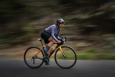 Helmeted cyclist riding a road bicycle past a blurred wooded hillside