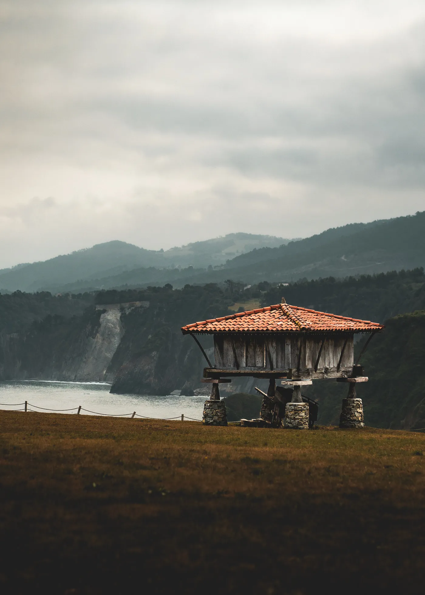 A small tiled-roof shelter overlooks the coast beneath low clouds.