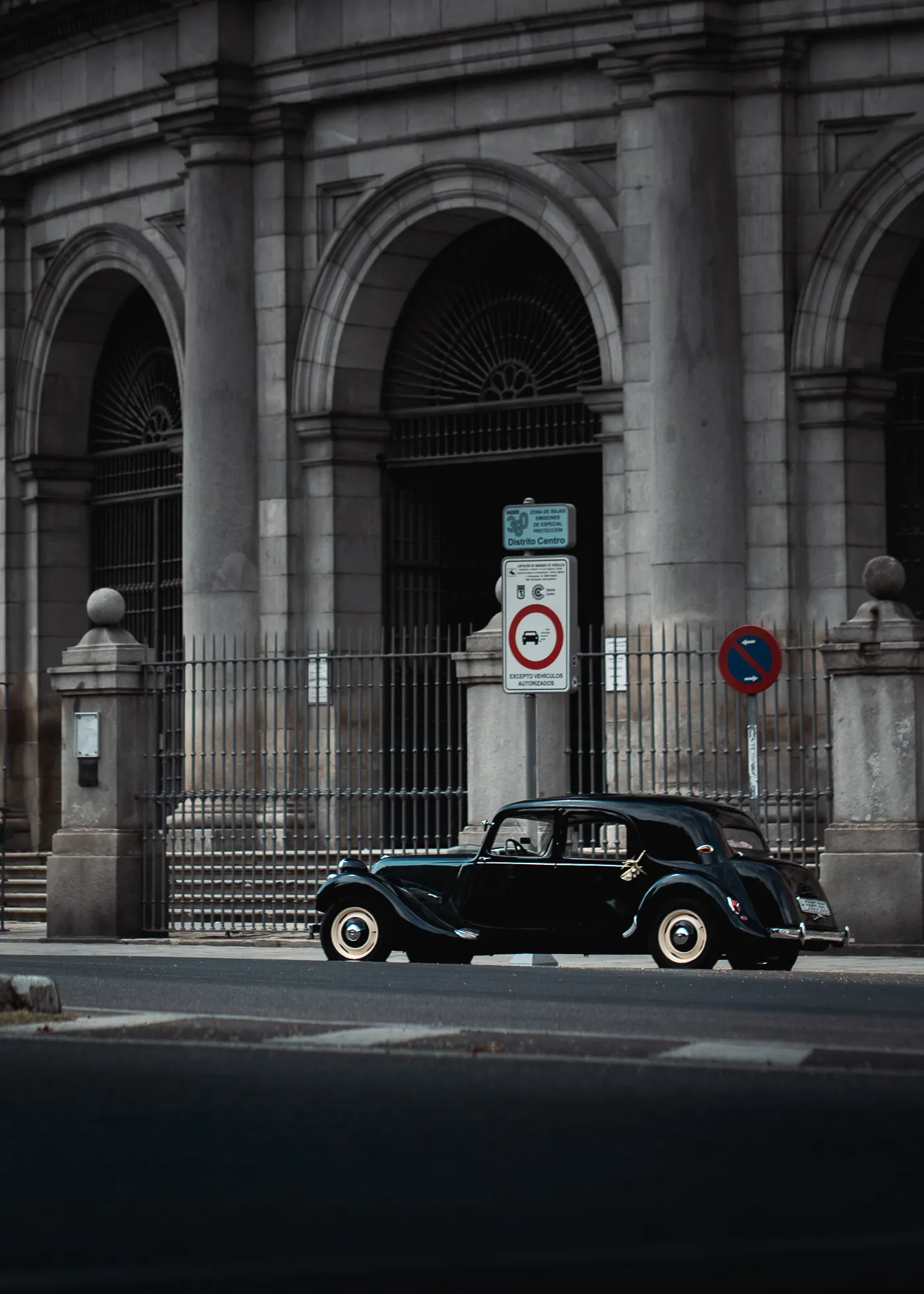 A dark vintage car passes an arched stone doorway.
