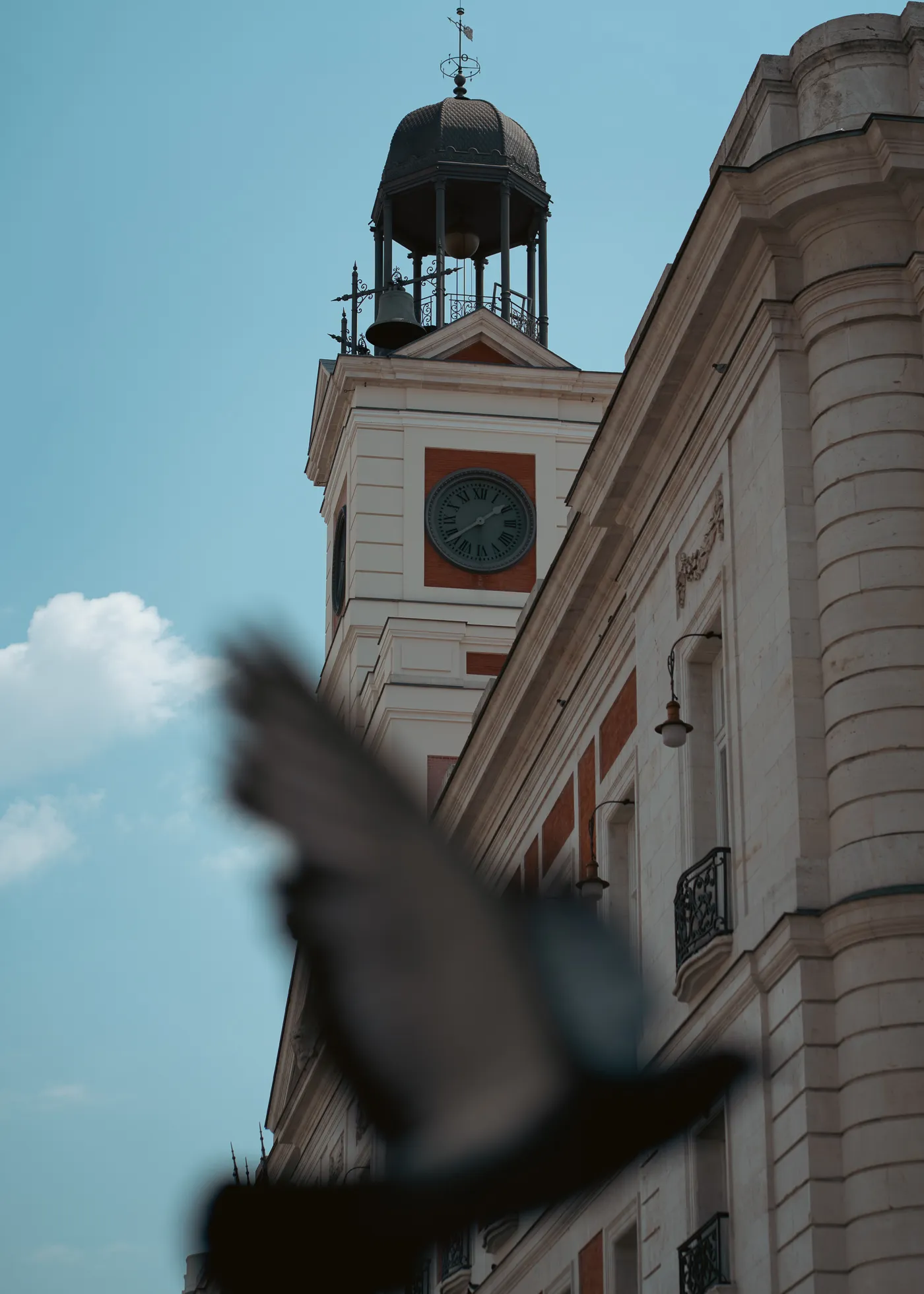 A bird passes in front of a clock tower against a blue sky.