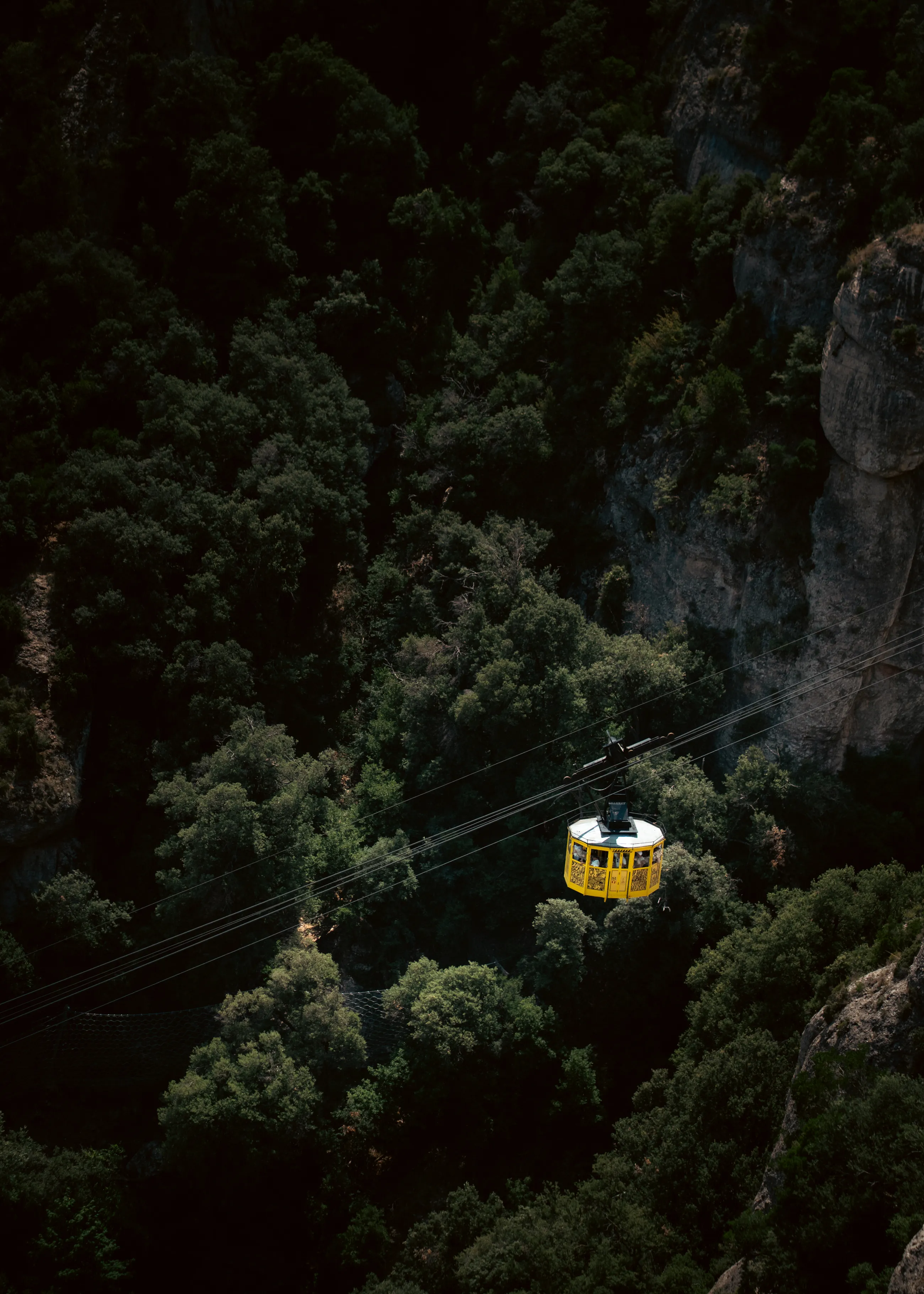 A yellow cable car hangs above a wooded gorge and rocky cliffs in Montserrat.