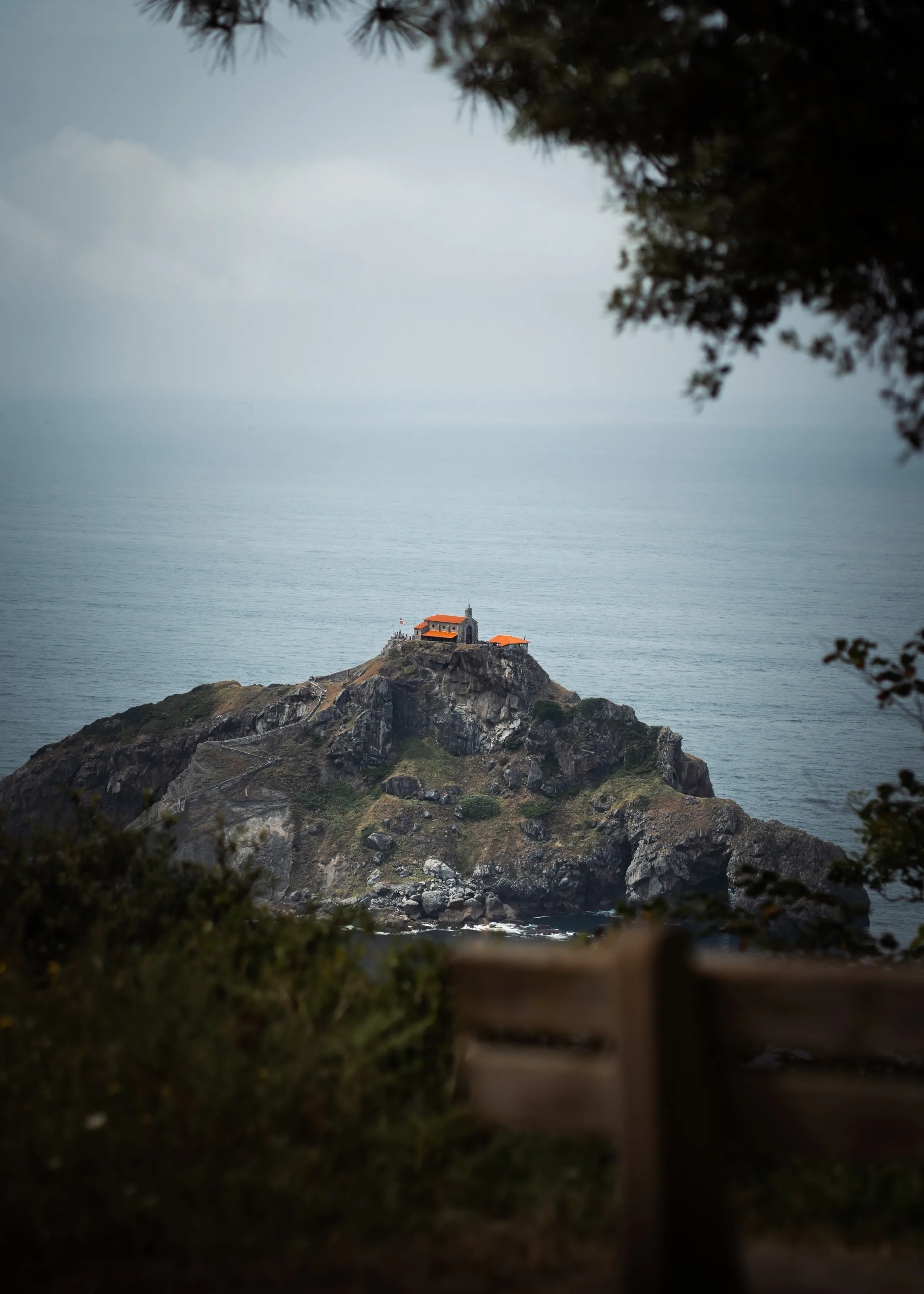 A rocky island and its small building are framed by coastal trees.