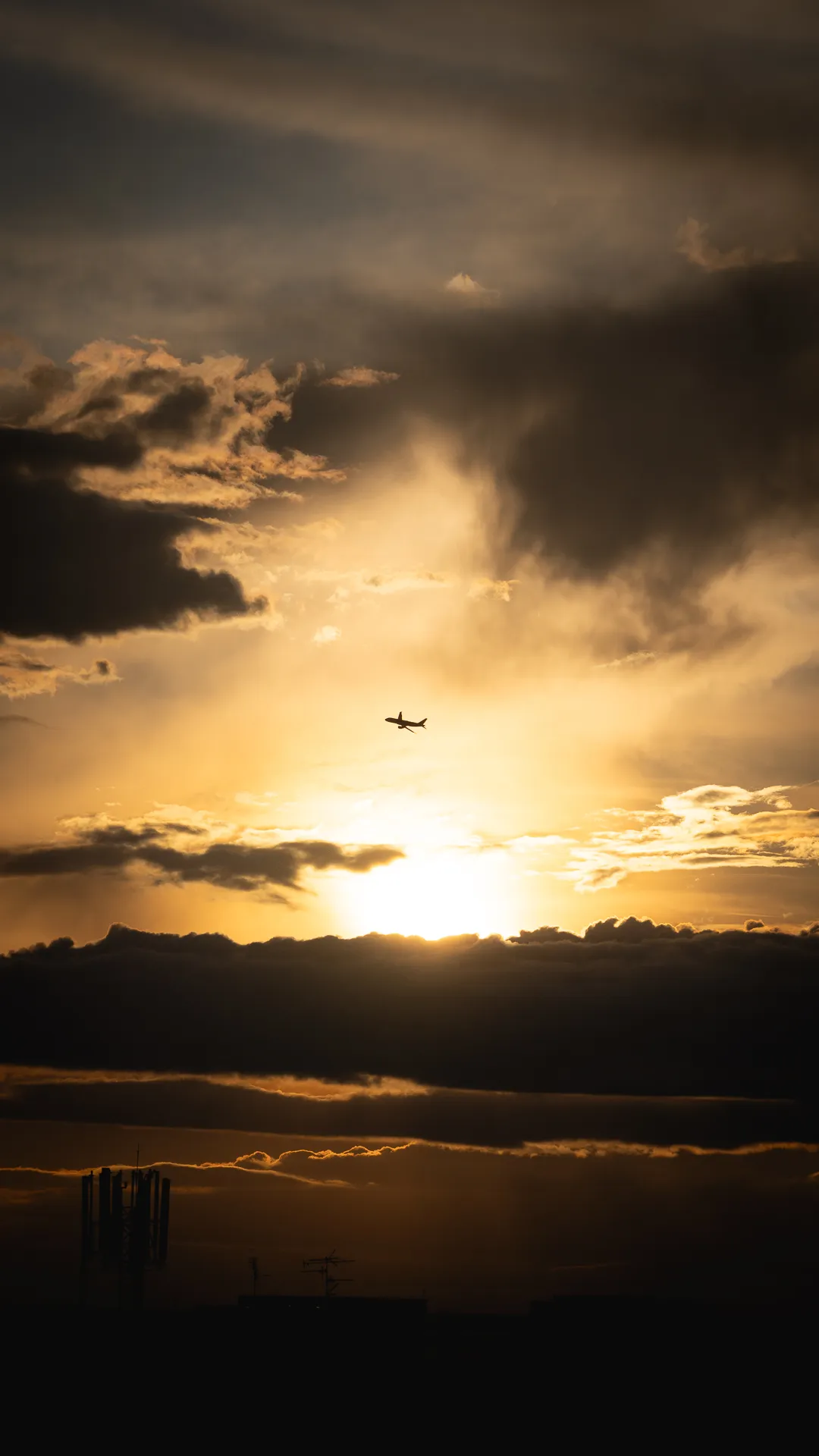 An aircraft crosses a golden sunset above dark mountains.