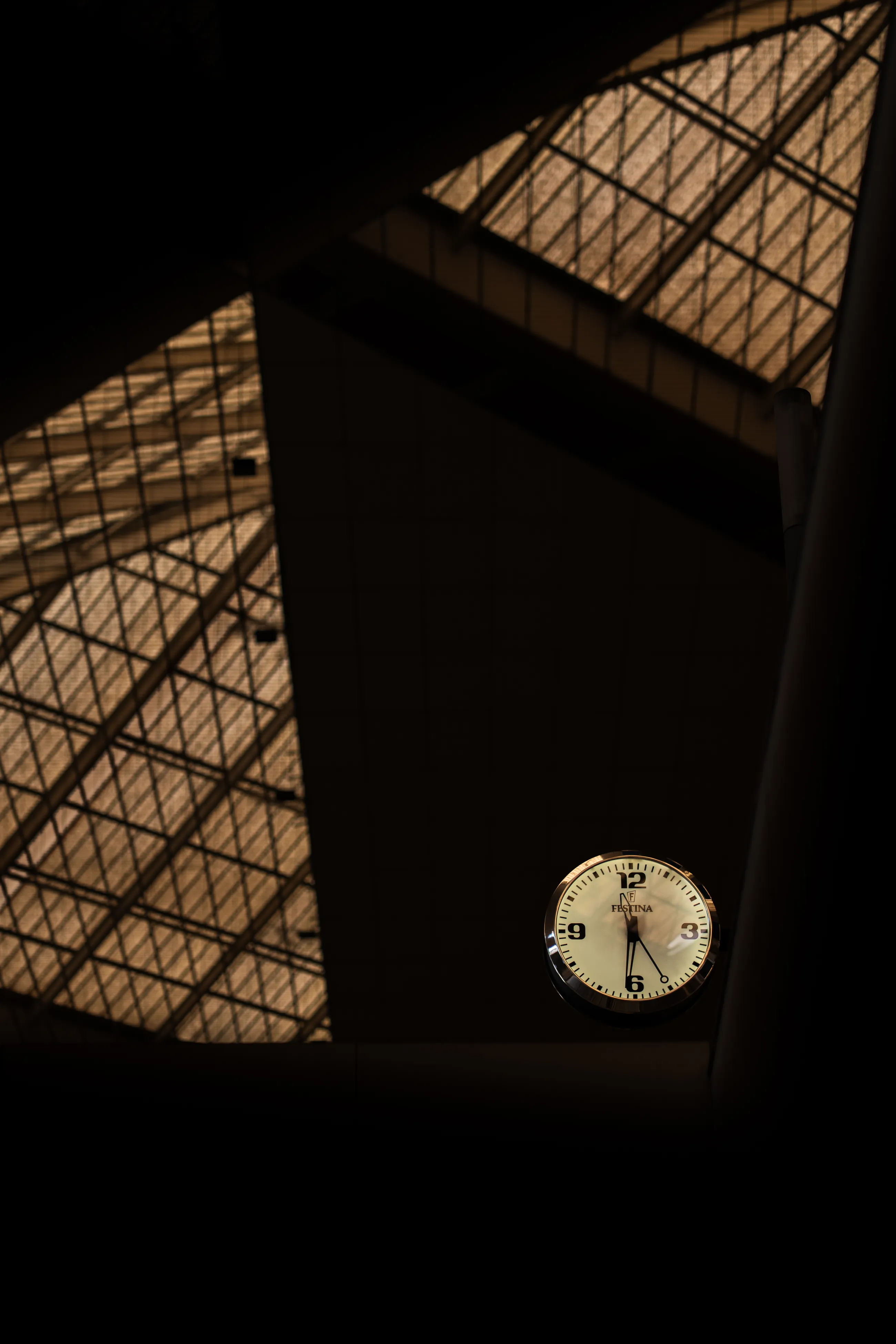 A station clock sits beneath angular skylights in warm light at Zaragoza Delicias.